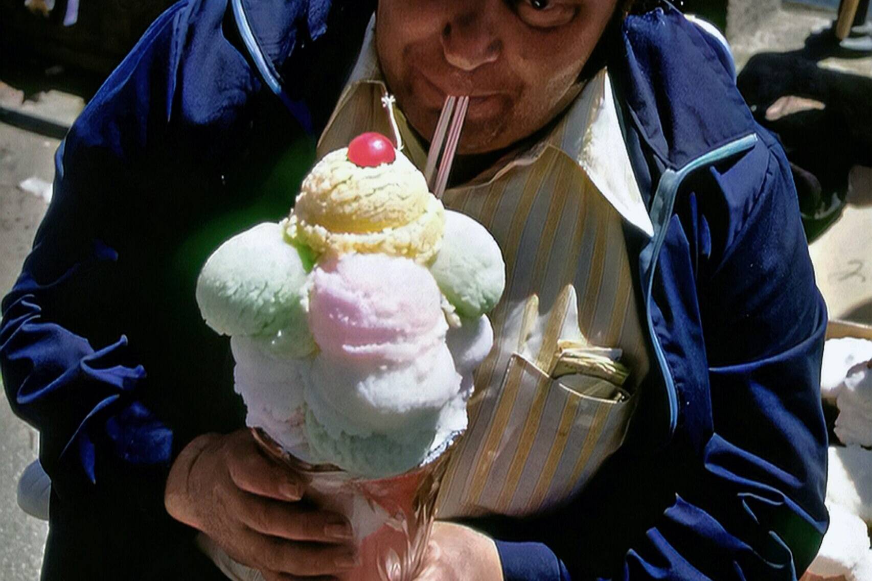 Man in blue jacket eating a giant ice cream